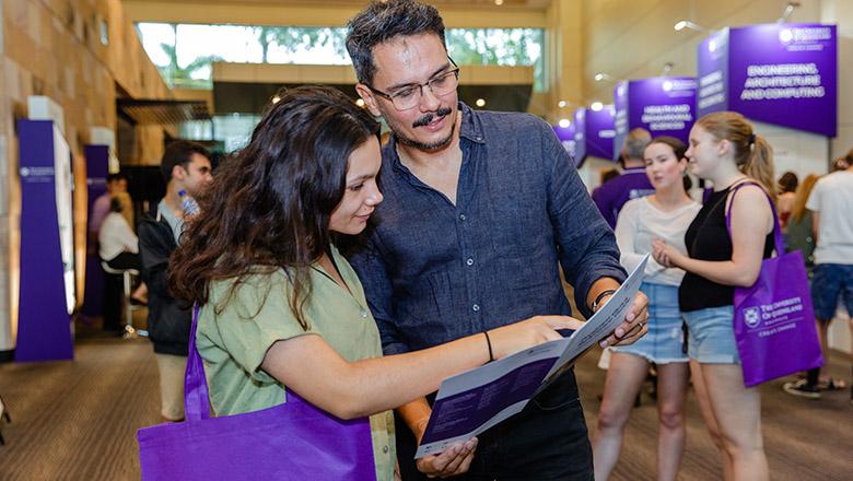 Father with teenage daughter look at brochure together at UQ event