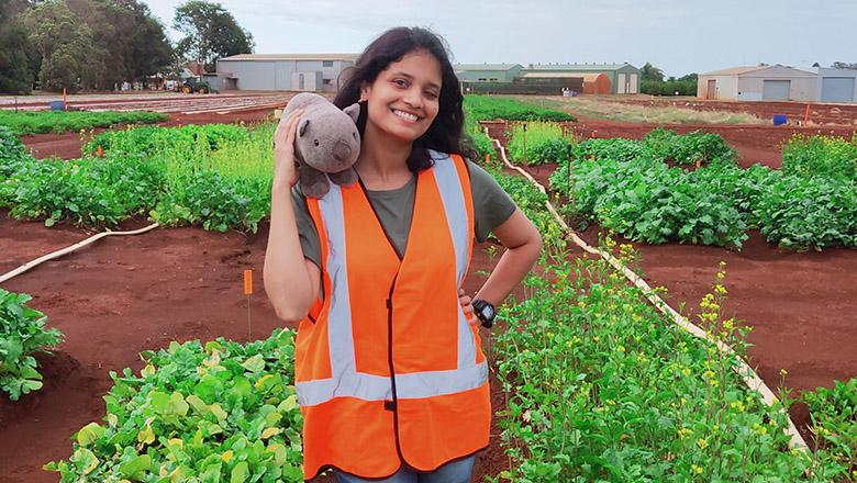 UQ Agribusiness graduate Gayathri Rajagopal holds a stuffed wombat toy in front of a field of crops
