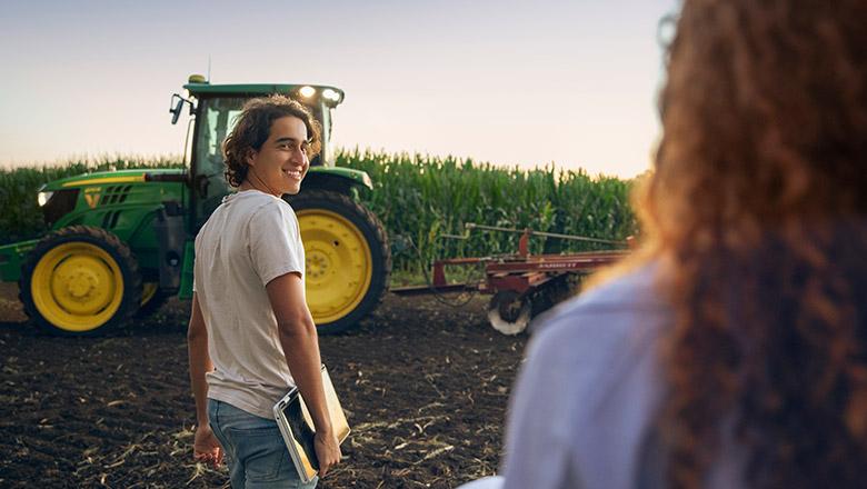 A UQ student stands in front of a tractor with a field of crops in the background