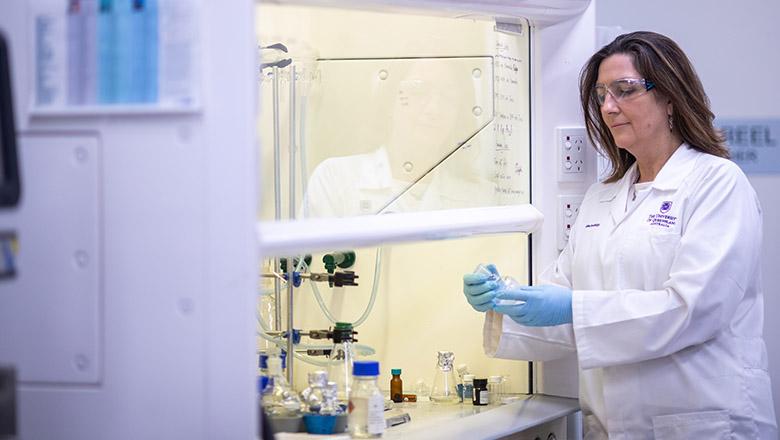 Professor Avril Robertson stands in white lab coat examining bottle with gloves on