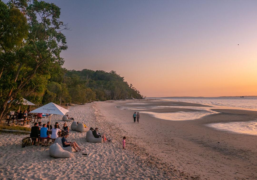 A group of people watching the sun set on the sand at Fraser Island. Image credit: Tourism & Events Queensland