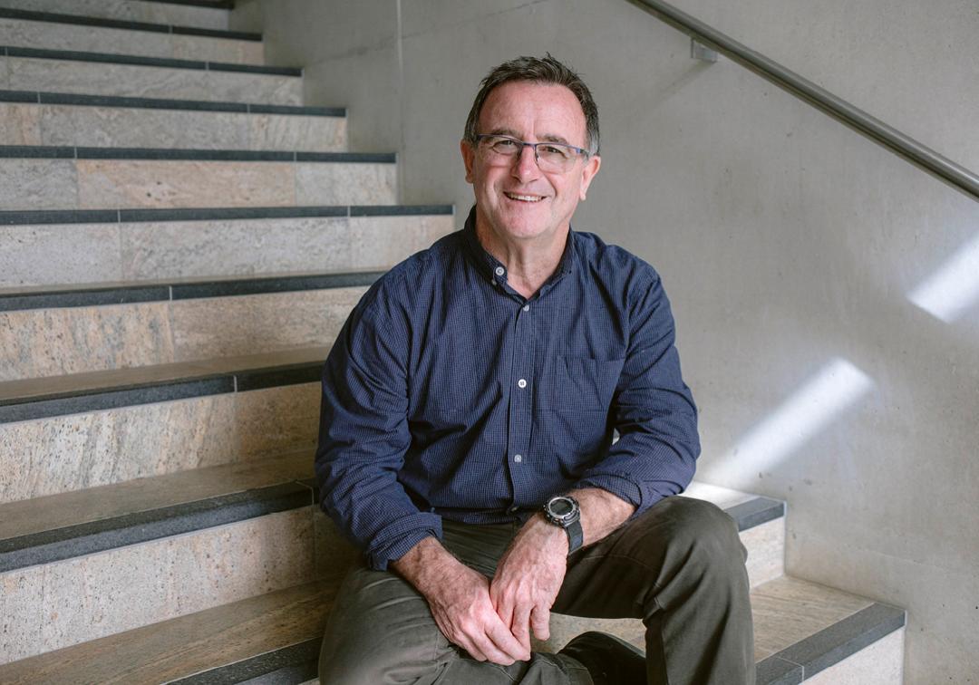 Associate Professor Ron Johnstone sits on a stone staircase smiling