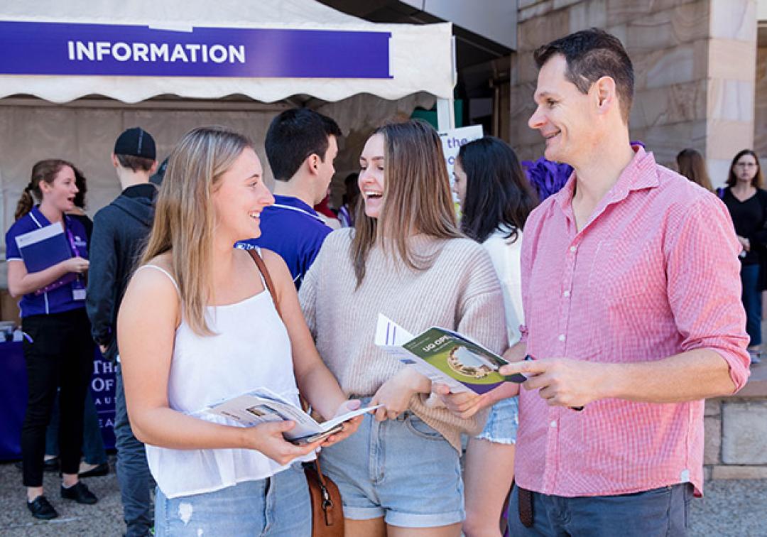 A father stands outside the information tent at UQ Open Day with his two daughters, looking at a program and chatting