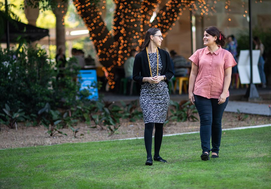 Professor Marta Indulska and Dr Ida Asadi Someh walk and talk through UQ's great court with fairy lights woven around a large tree in background