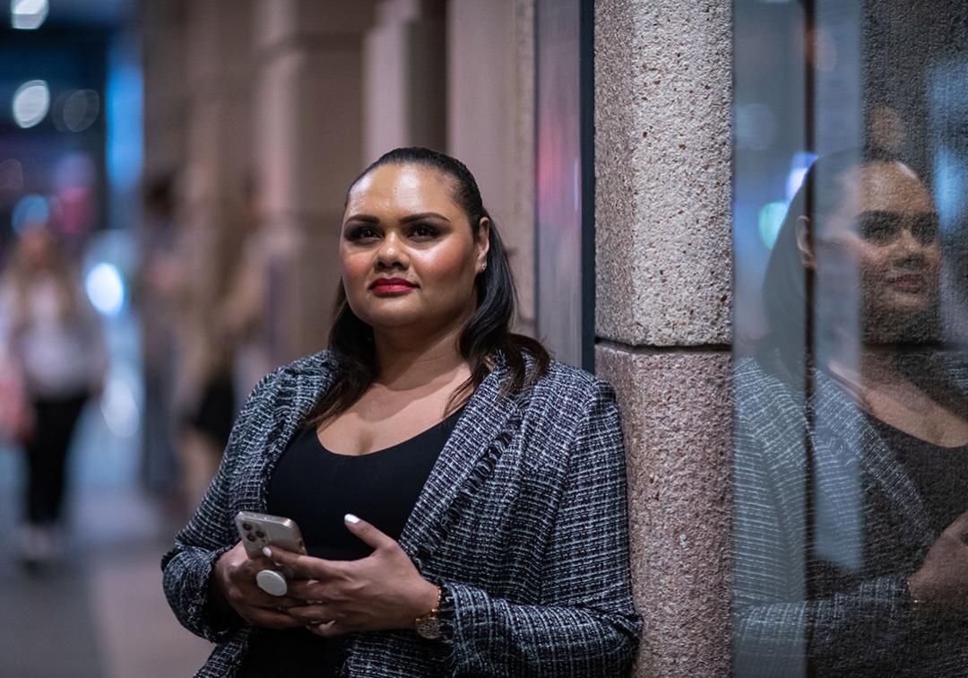 UQ Law Graduate Jahmillah Johnson stands holding a smartphone, reflected in a glass panel