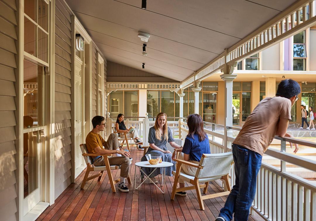 Students gather on the porch of a Queenslander, sitting in deck chairs