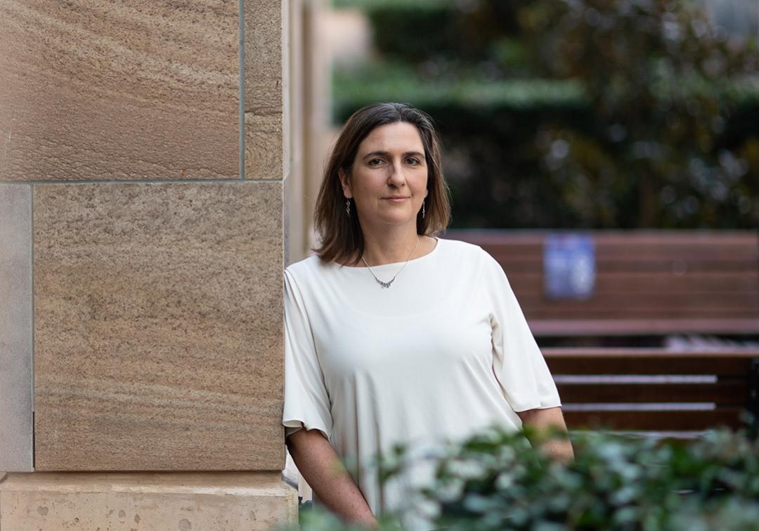 Professor Avril Robertson stands leaning against sandstone building
