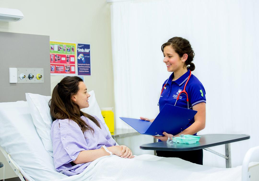 A UQ student nurse stands by the bedside of a patient in a hospital