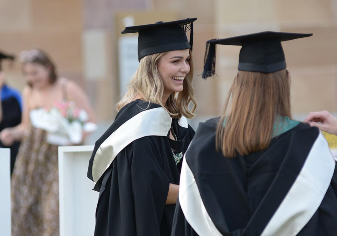 Two young women wear graduation gowns and mortarboards 