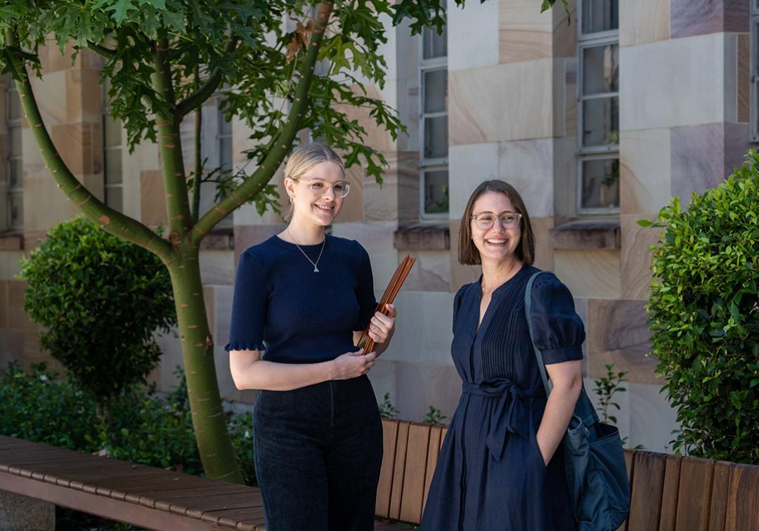 Rose Foster and Justine Bell-James stand smiling in front of UQ's sandstone buildings