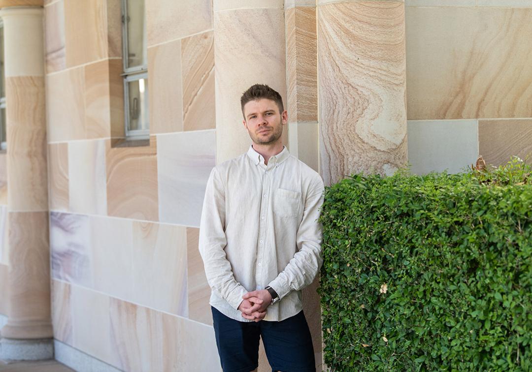 Sam Hislop-Lynch stands in front of a sandstone building in UQ's Great Court