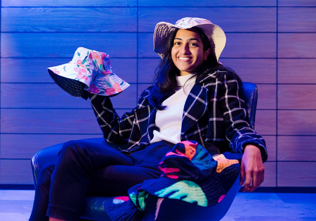 Arts/Law graduate Famin Ahmed seated on a chair holding her handmade hats.