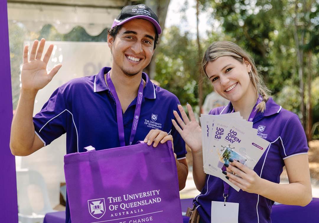 UQ Students in purple polo shirts hold leaflets and a UQ tote bag and wave at the camera