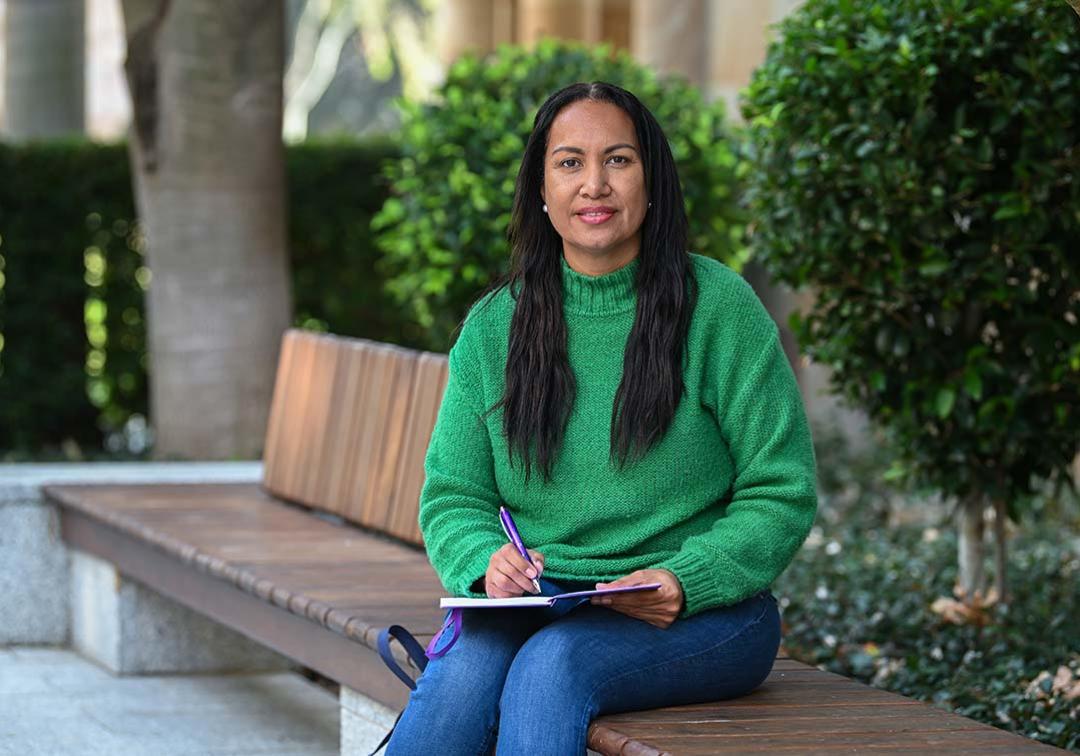 UQ Social Work student Jaala Ozies sits on a bench, writing in a notebook