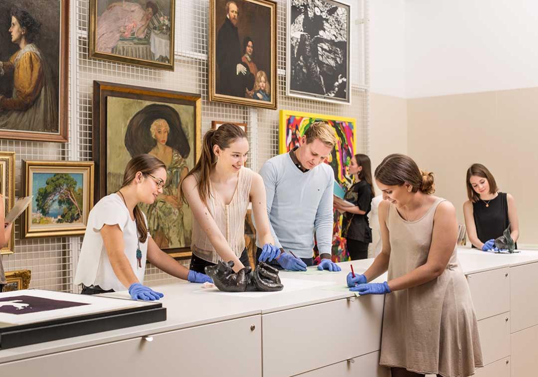 A group of students inspect pieces of art with gloves on