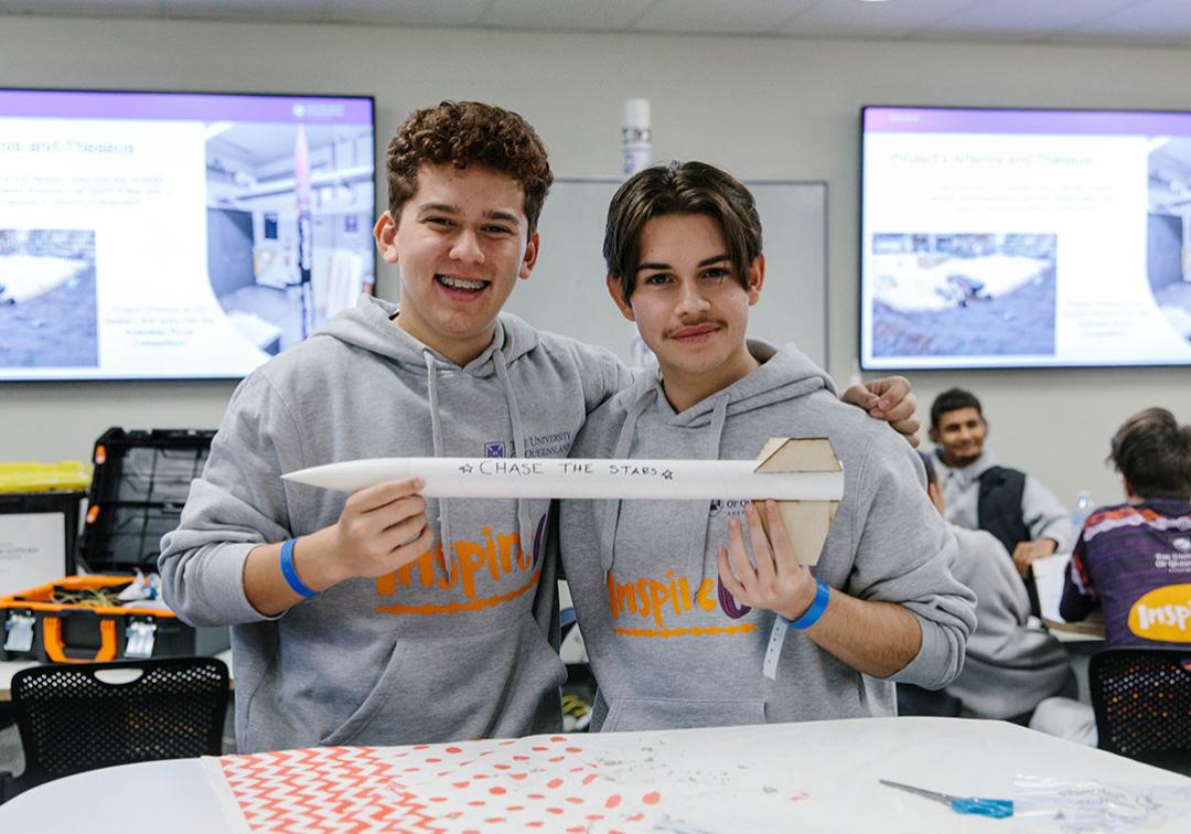 Two InspireU students holding a small cardboard rocket that says 'Chase the stars'