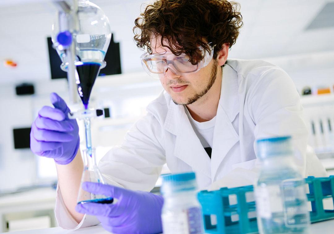 UQ chemistry student looks at blue liquid in a beaker