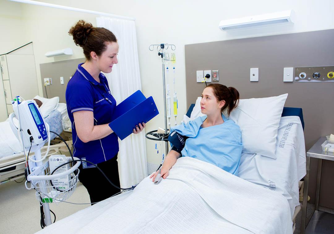 A UQ nursing student talks to a patient in a hospital bed