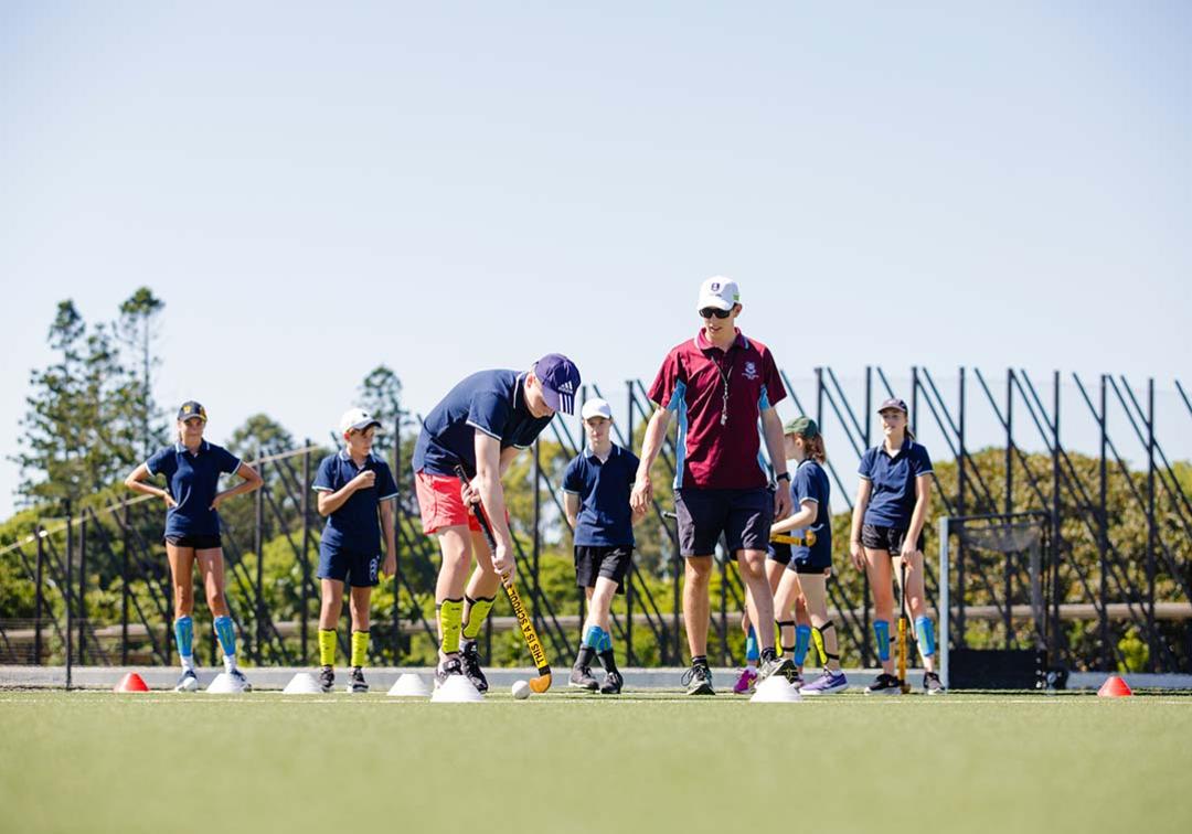 A UQ physical education student teaches a school students how to play hockey