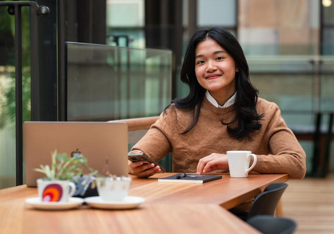 A girl sitting with her laptop and a coffee