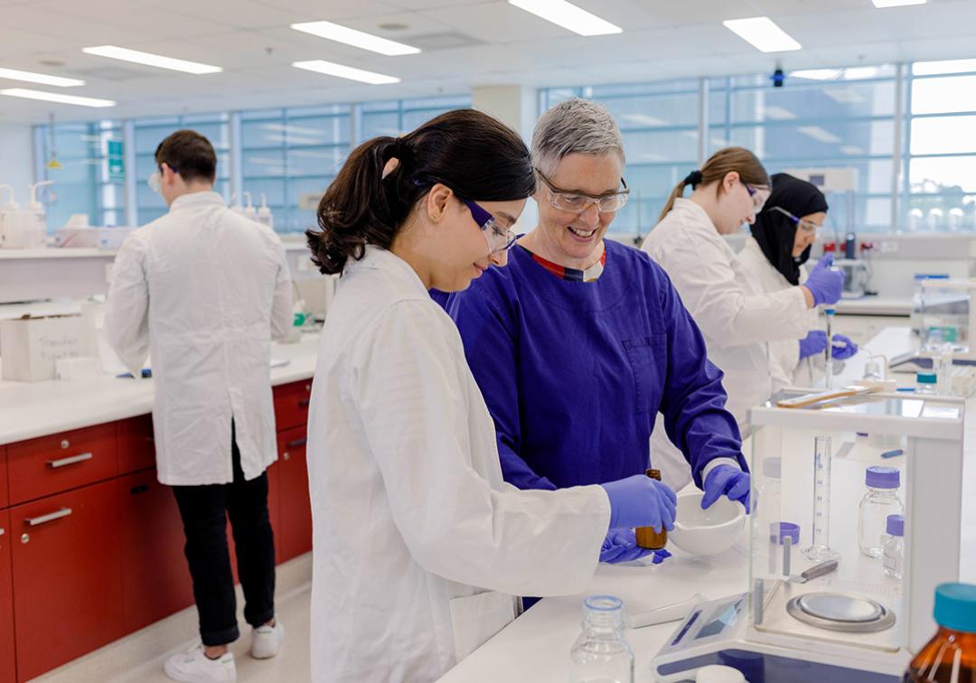 A UQ pharmacy teacher and student dispense medicine into a mortar and pestle in a lab