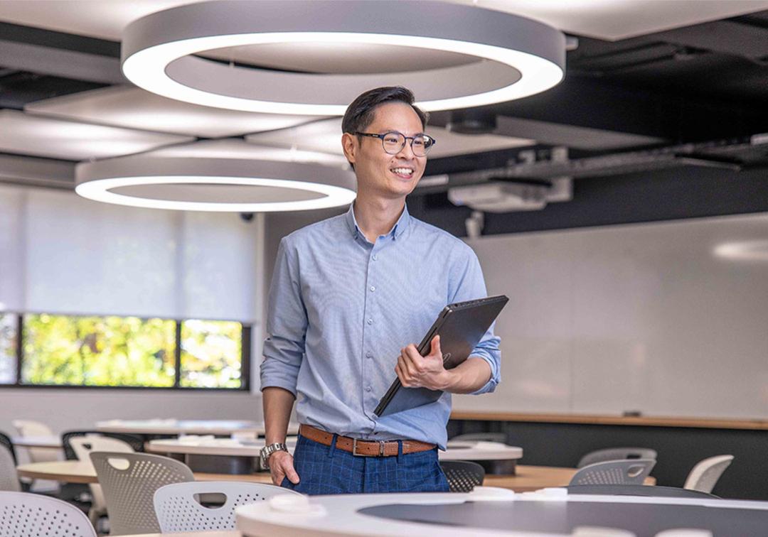 Man holding laptop in brightly lit classroom