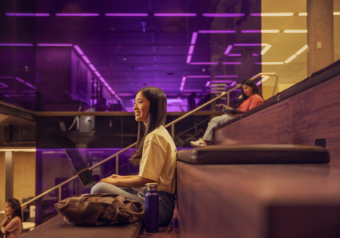 UQ student sitting inside on steps with laptop looking fondly into the distance