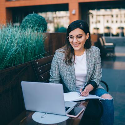 Young professional woman in blazer working on laptop outside