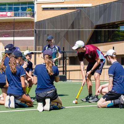 PE teacher demonstrating how to play hockey to high school students