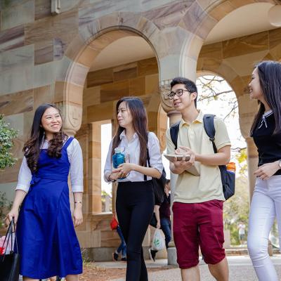 Four students walking through sandstone arches at the St Lucia campus.