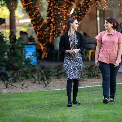 Professor Marta Indulska and Dr Ida Asadi Someh walk and talk through UQ's great court with fairy lights woven around a large tree in background