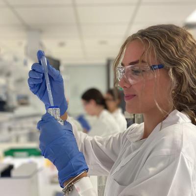 Female student in research lab wearing science glasses and lab coat. 