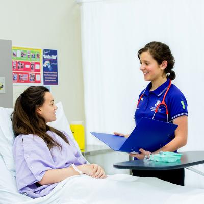 A UQ student nurse stands by the bedside of a patient in a hospital