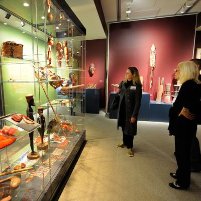 Three people stand looking at a museum display of Indigenous artifacts