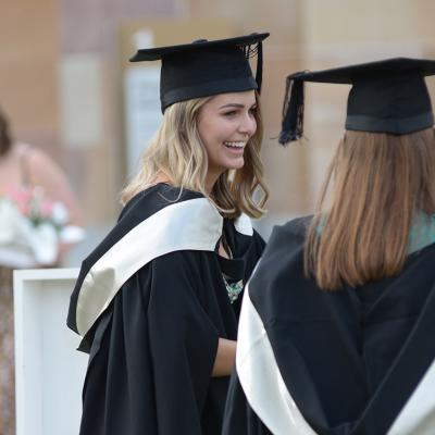 Two young women wear graduation gowns and mortarboards 