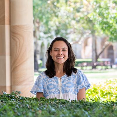 Barbara Azevedo de Oliveira stands smiling in UQ's Great Court, flanked by sandstone and trees