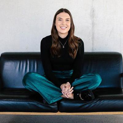 UQ Student Sylvia Stuen-Parker sits cross-legged on a black leather couch, smiling at the camera
