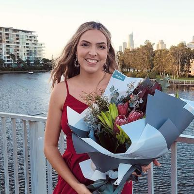 Image of Nicole Petzer standing in front of the Brisbane River with flowers after graduation 