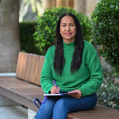 UQ Social Work student Jaala Ozies sits on a bench, writing in a notebook