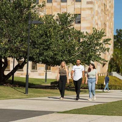 Students walking on a path at UQ's St Lucia campus with sandstone buildings in background