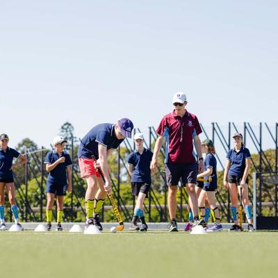 A UQ physical education student teaches a school students how to play hockey