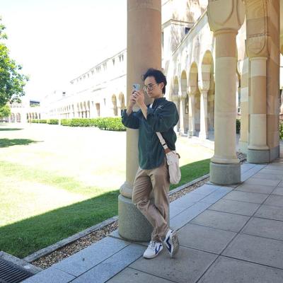 Male student leaning on a cloister taking a photo with his phone