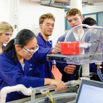 A group of UQ engineering students in lab coats and safety glasses inspect an experiment