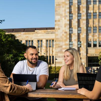 UQ students studying at a picnic table in front of sandstone buildings