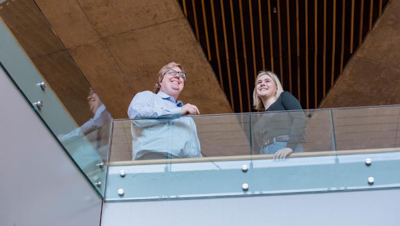 Professor Alastair Blanshard and UQ humanities student, Amelia, stand behind a glass bannister smiling 
