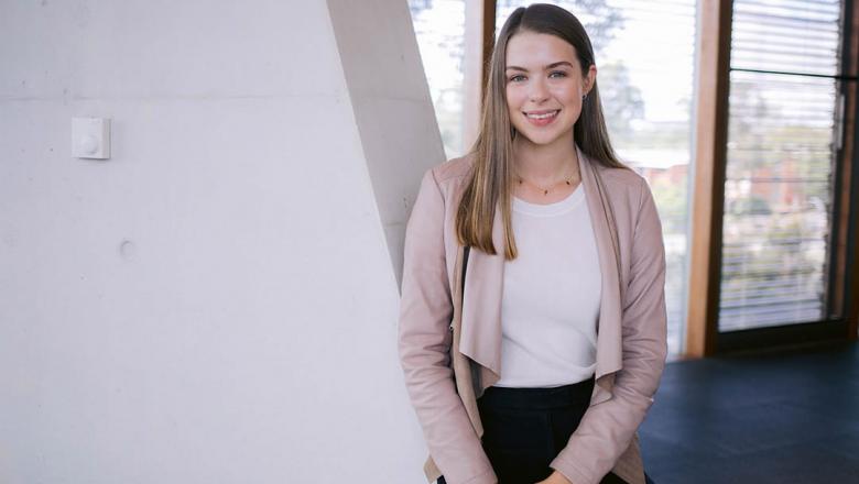 UQ Engineering student Caitlin Reid leans against a white wall, smiling