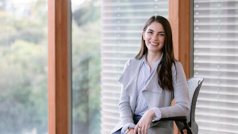 UQ Engineering graduate Tierney George sits in a chair smiling in front of a window with blinds