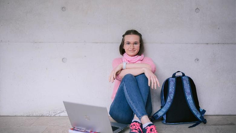 UQ Social Work student Heidi Davis sits cross-legged leaning against a concrete wall with an open laptop on one side and a backpack on the other