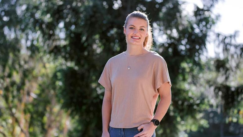 Former UQ student Laura Benn stands smiling at the camera in front of blurred greenery