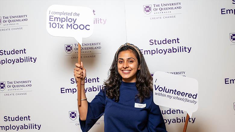 A UQ student stands holding signs that say 'I completed the Employ 101xMOOC' and 'I volunteered within my school/faculty'